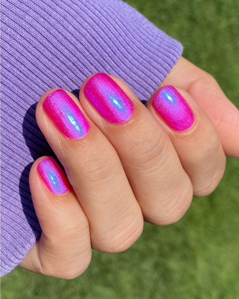 Fingers curled up on purple sleeve to show shimmery hot pink neon nails with iridescent glow.