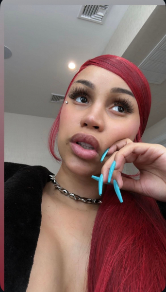 Cardi B takes a selfie with bright red hair and vivid aqua blue nails.