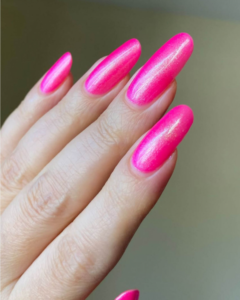 Long shimmery roundedtip hot pink acrylic nails point up and out.
