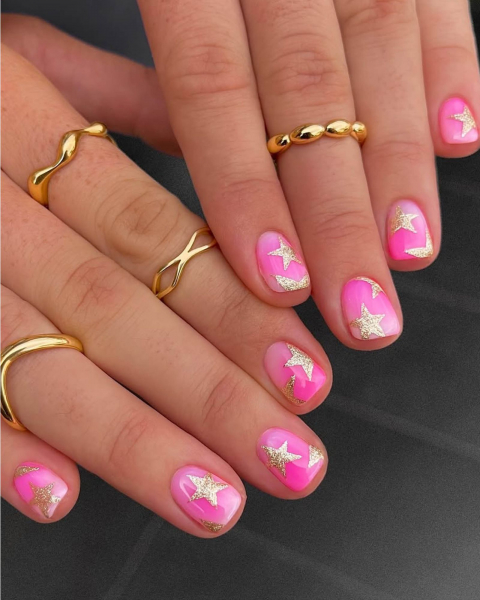 Sparkly gold stars on short hot pink ombre nails.